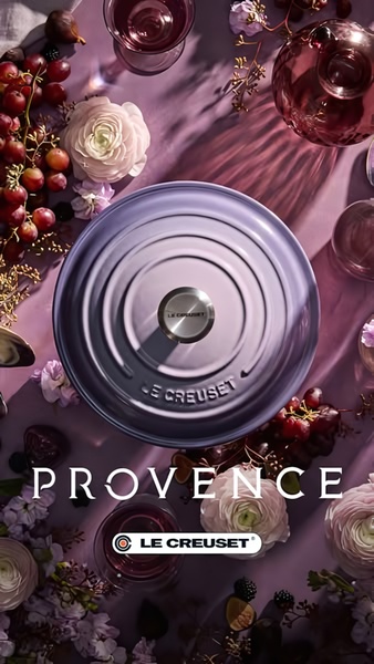 A top-down aesthetic shot of a lavender Dutch oven surrounded by seasonal produce and floral arrangements on a mauve linen backdrop.
