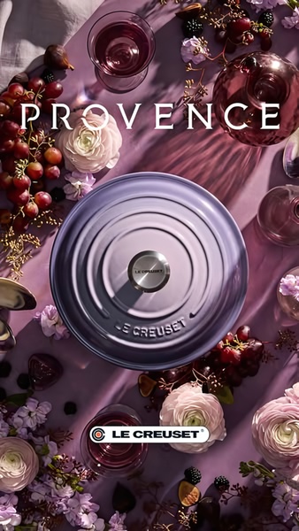 A high-end, top-down flat lay featuring a purple cast iron dutch oven surrounded by grapes, figs, and floral arrangements in a monochromatic lavender palette.