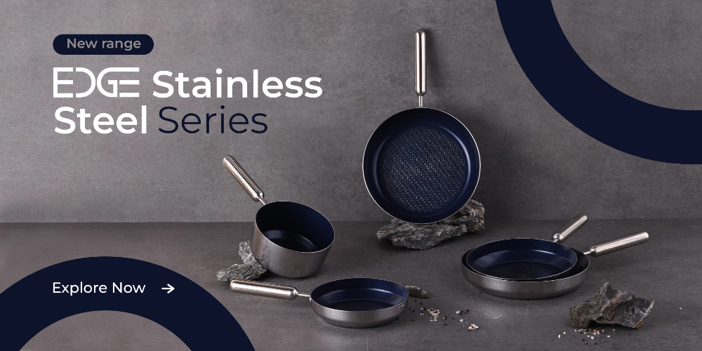 A high-end product hero advertisement showcasing a four-piece stainless steel pan set arranged on a textured stone surface with a dark blue circular accent.