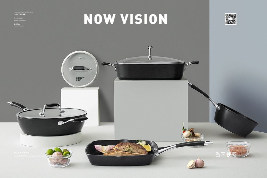 A high-end studio shot of a black cookware set arranged on white pedestals against a two-tone grey and blue background.