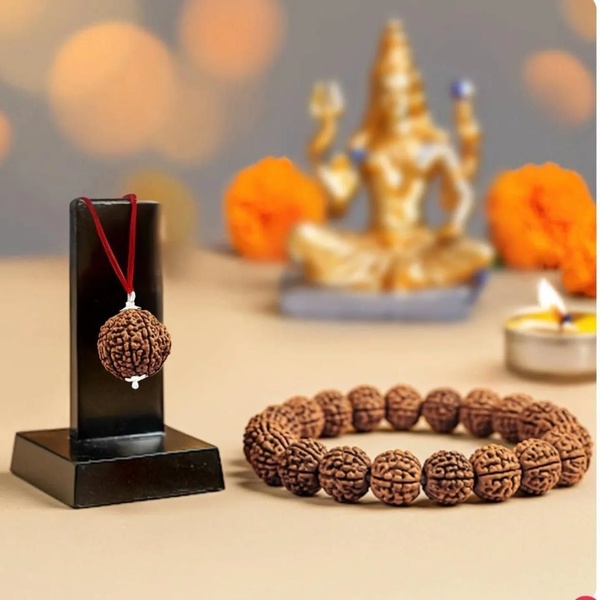 A high-quality still-life product photo featuring a Rudraksha bead pendant on a stand alongside a matching bead bracelet, with a soft-focus deity statue in the background.