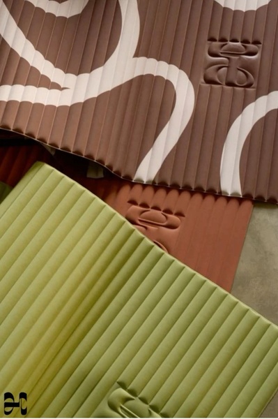 A close-up aesthetic shot showcasing the distinct pleated texture and logo detail of high-end yoga mats in olive, brown, and terra-cotta tones.