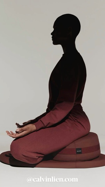 A high-contrast, minimalist studio photograph featuring a person meditating on a cushion, using deep red tones and soft lighting to evoke calm.