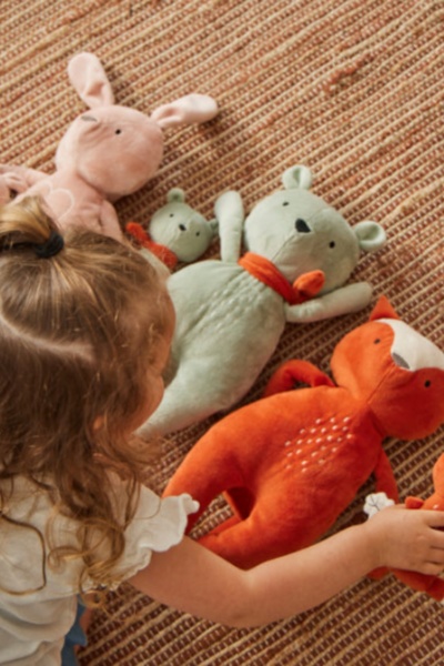 A close-up, top-down shot of a child interacting with several colorful plush toys on a natural, textured rug.