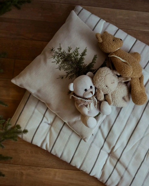 A high-angle product hero shot featuring three plush toys resting on a striped cushion, designed to evoke comfort and warmth.