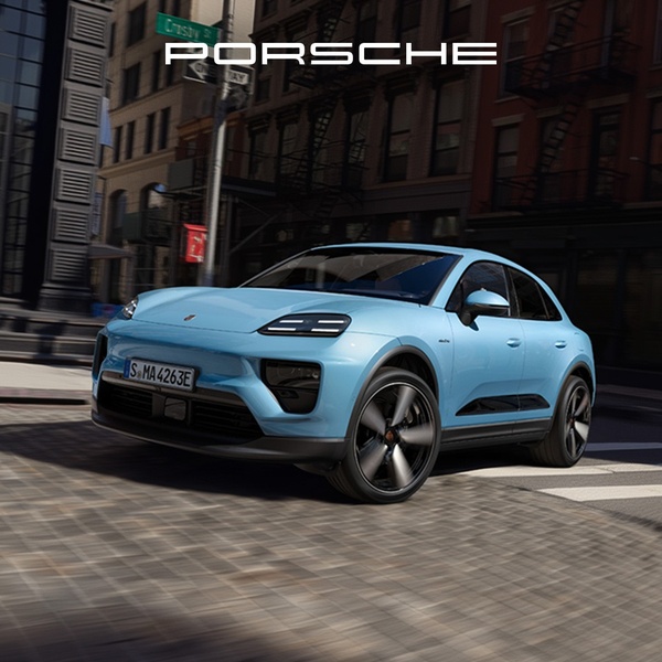 A high-angle, eye-level shot of an electric SUV driving through a city intersection at dusk, emphasizing motion blur and premium brand aesthetics.