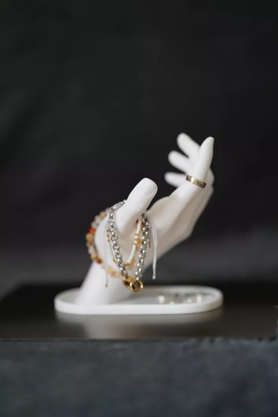 A clean, high-contrast shot of a white hand sculpture modeling a bracelet and gold ring against a dark background.