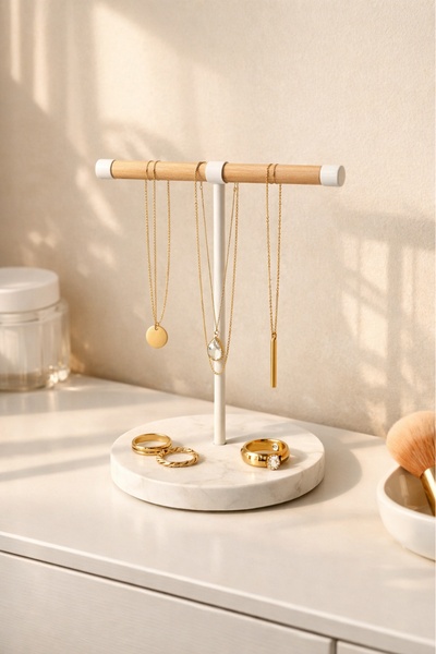 A clean, high-key studio shot of a wood and marble jewelry stand displaying delicate necklaces and rings.