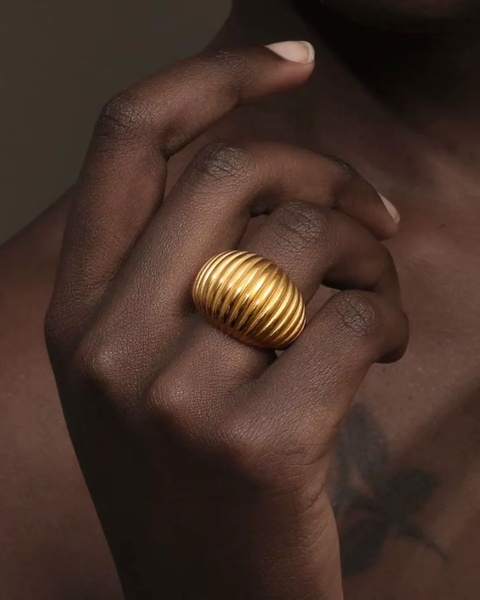 A close-up, high-contrast hero shot of a ribbed gold ring on a finger, focusing on texture and material quality.