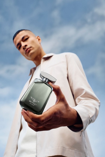 A close-up, low-angle perspective of a man holding a bottle of cologne against a sky backdrop, emphasizing the product with a sense of status and scale.