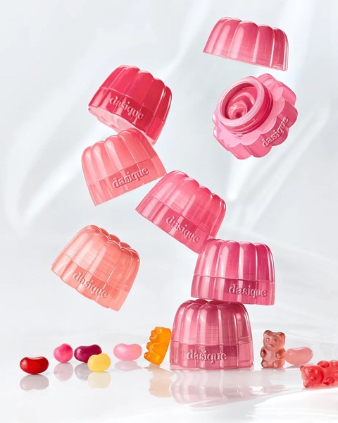 A visually striking product shot showing multiple jelly-textured skincare jars floating in mid-air above a scattering of gummy candies on a soft white background.