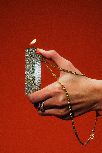 A high-contrast, professional studio shot of a diamond-encrusted lighter being held by a hand against a solid, intense red background.