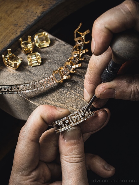 A close-up shot of an artisan's hands meticulously setting diamonds into a gold ring frame.