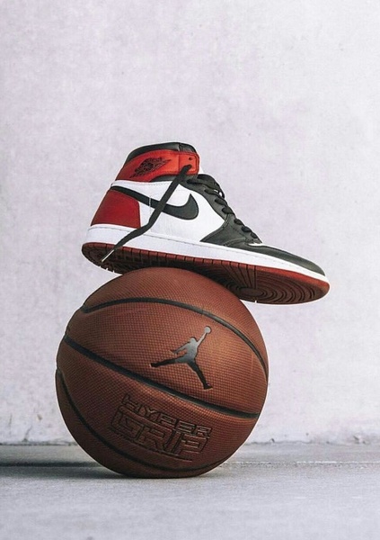 A high-contrast studio shot featuring a basketball sneaker balanced perfectly on top of a textured basketball.