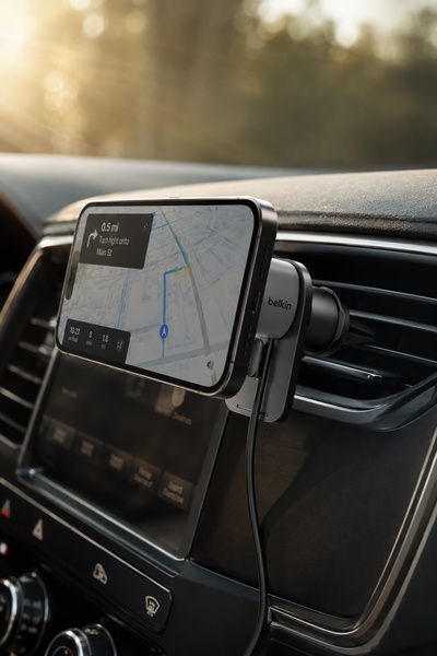 A close-up, high-quality shot of a car phone mount securely holding a smartphone displaying navigation, positioned in a car air vent during golden hour.