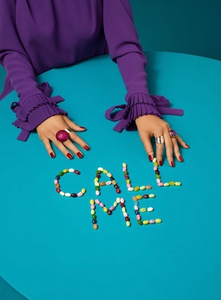 A close-up shot of hands wearing rings and gesturing over a blue table where candy spelling the words CALL ME is laid out.