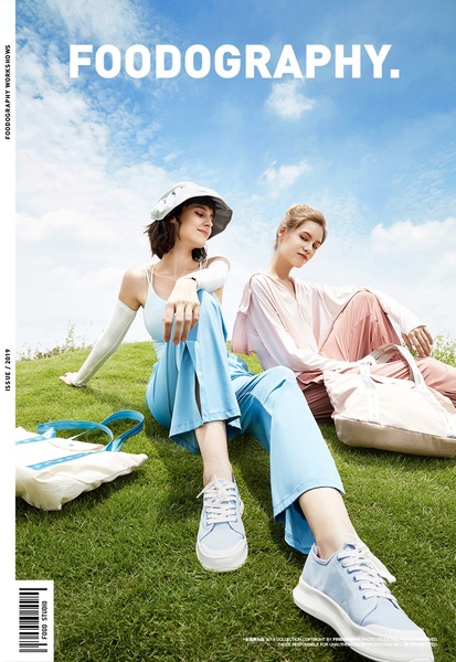 A high-key, outdoor lifestyle shot of two models in casual wear and matching sneakers on a grassy hill, emphasizing a clean and airy brand identity.