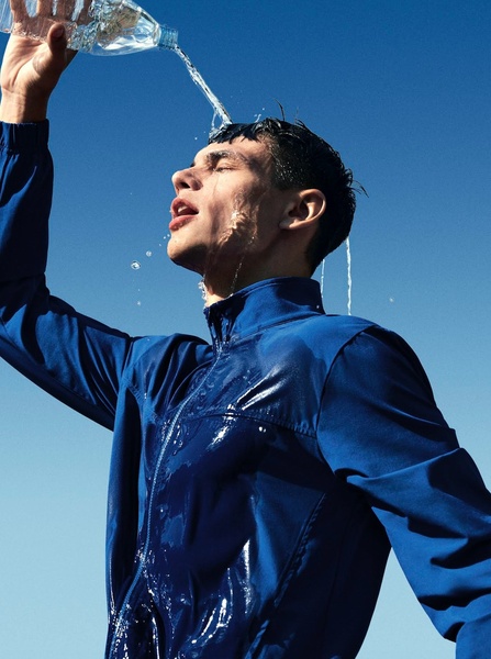 A close-up shot of an athlete pouring water over their head while wearing a performance jacket, emphasizing cooling and relief.
