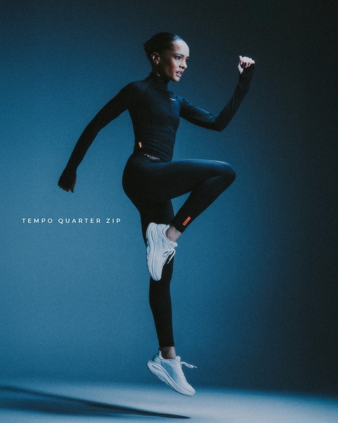 A high-contrast, studio-lit image of an athlete mid-air, emphasizing the sleek form-fitting design of the product against a clean blue background.