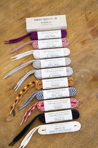 A high-angle, organized display of assorted shoelace pairs in branded, minimalist packaging laid out on a rustic wooden table.