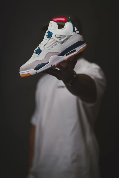 A high-contrast, moody shot featuring a hand presenting a white and blue running shoe against a dark, minimalist background.