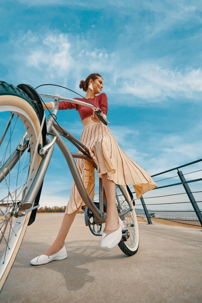 A woman riding a bicycle against a bright blue sky, wearing comfortable walking shoes, effectively blending lifestyle photography with product placement.