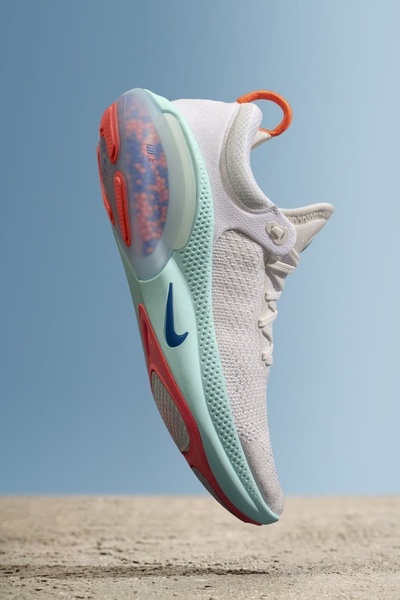 A clean, studio-lit shot of a white running shoe suspended against a soft blue background, emphasizing its design and vibrant color accents.