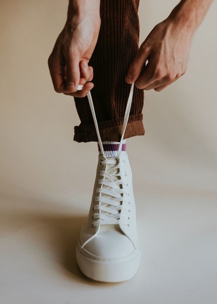 A close-up, centered product shot of a high-top sneaker being tied, focusing on texture and material detail against a neutral background.