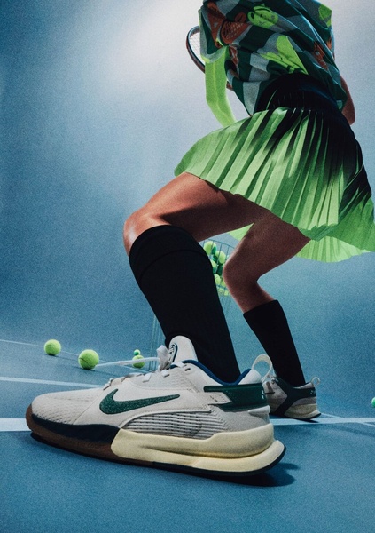 A high-energy, low-angle perspective shot of a tennis player mid-movement, emphasizing the design and grip of the performance shoe against a blue court.