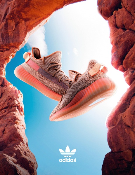 A high-contrast, vertical hero shot of a running shoe floating between two rock formations against a clear blue sky.