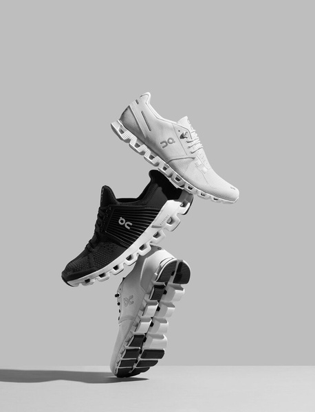 A high-end studio shot featuring three running shoes stacked vertically against a neutral grey background, emphasizing product design and clean aesthetics.