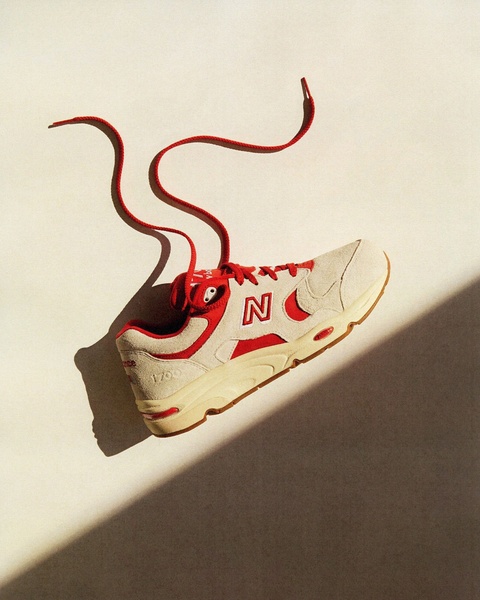 A high-contrast studio photograph of a New Balance 1700 sneaker floating against a neutral background, highlighting the product with dramatic side-lighting.