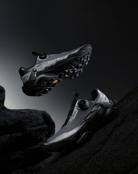 A high-end product display featuring two running shoes floating against a dark, volcanic textured background to emphasize performance and design.