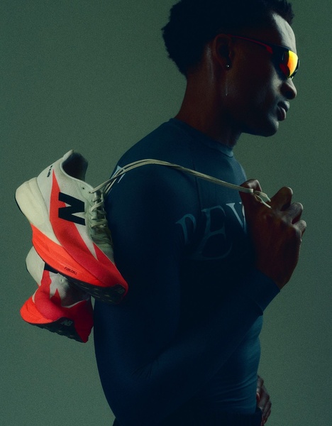 A high-contrast, moody studio shot featuring a running shoe draped over a model's shoulder, focusing on silhouette and premium design details.