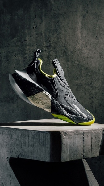 A high-contrast, studio-style product shot of a running shoe placed on a concrete block, emphasizing form, texture, and neon accents.
