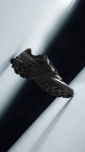A high-end studio shot of a black running shoe angled against a clean, geometric background, emphasizing form and texture.