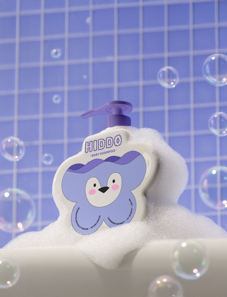 A high-quality studio product photo of a uniquely shaped baby shampoo bottle surrounded by soft, realistic soap bubbles against a clean tiled background.