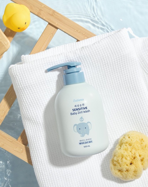 A high-key, overhead shot of a Baby 2in1 Wash bottle resting on a white towel, surrounded by water and a rubber ducky, emphasizing gentle care.