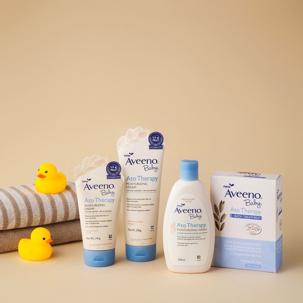 A clean product hero display of Aveeno Baby Ato Therapy skincare line, featuring bath-time elements like rubber ducks and towels to reinforce the product utility.