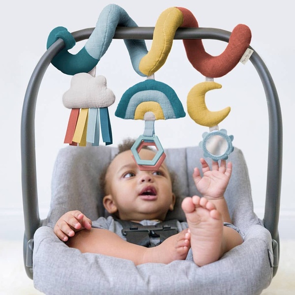 A close-up, high-key shot of an infant interacting with a multi-textured, rainbow-themed spiral toy attached to a stroller handle.