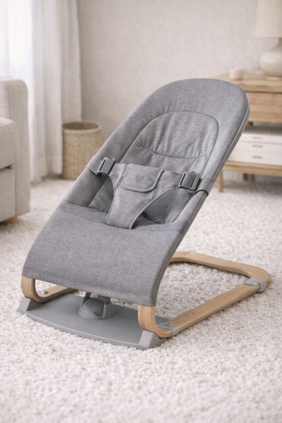 A high-quality, studio-lit photograph of a neutral-toned baby bouncer placed in a cozy home environment, emphasizing comfort and premium build quality.
