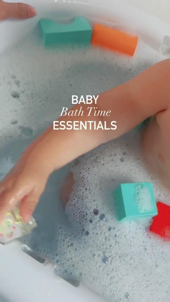 A close-up, top-down shot of a baby in a soapy bath with colorful floating toy blocks, focusing on bath time routine.