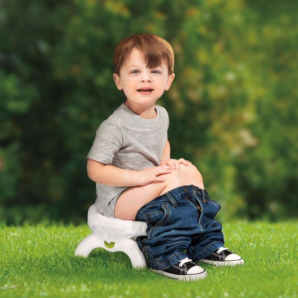 A candid, bright, and relatable shot of a toddler successfully using a portable potty seat outdoors in a natural setting.