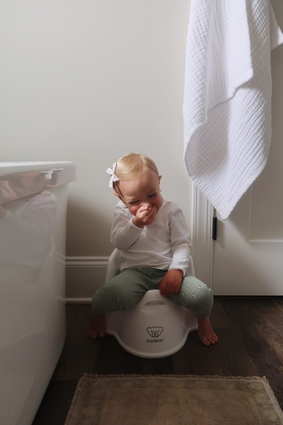 A natural, unposed photo of a toddler laughing while using a training potty, emphasizing a relatable milestone in a home setting.