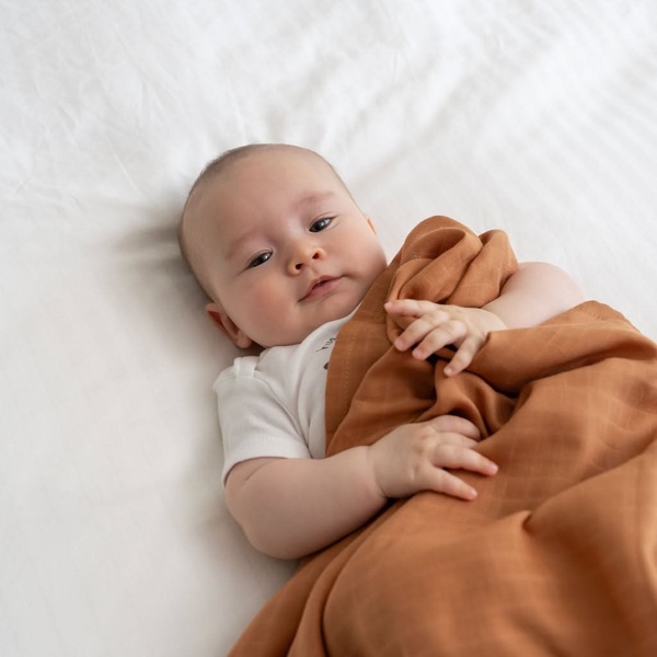 baby swaddle, receiving blanket, muslin swaddle, baby blanket, swaddling cloth, product demo, lifestyle, calm, warm, neutral, brown