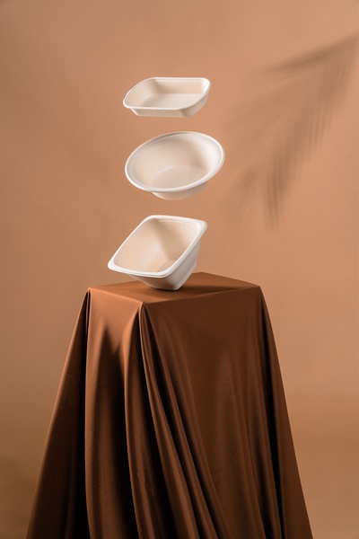 A clean, studio-lit creative featuring three stacked disposable bowls suspended in air over a draped silk stand, creating a premium visual effect.