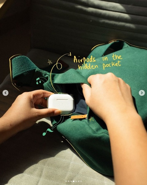 A close-up shot showing a hand placing headphones into a hidden pocket of a green tote bag, highlighted with hand-drawn annotations.