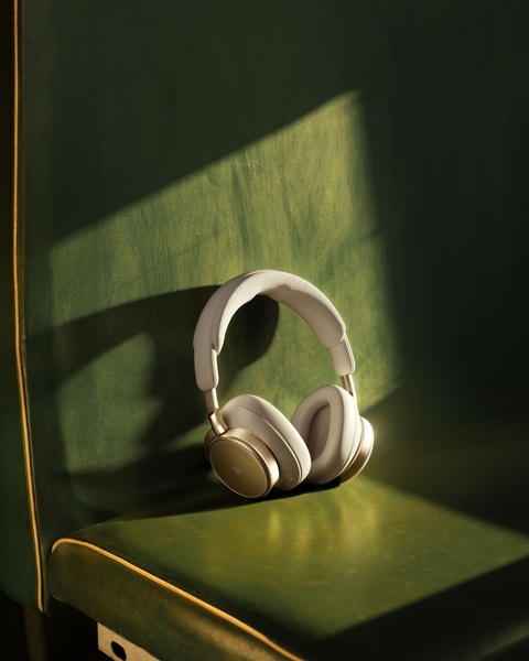 A pair of premium over-ear headphones rests against a deep green leather backdrop, illuminated by high-contrast natural sunlight.