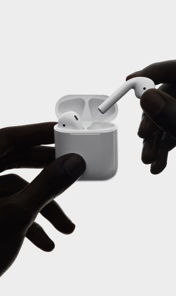 A high-contrast, minimalist shot showing hands interacting with a pair of wireless earbuds and its charging case.