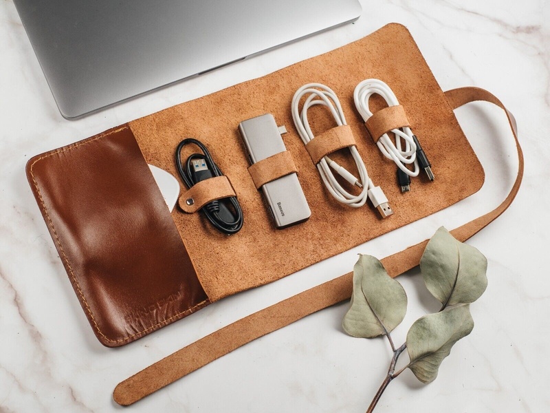 A high-quality top-down shot of a leather cable roll-up case holding tech accessories, emphasizing premium material and organizational efficiency.
